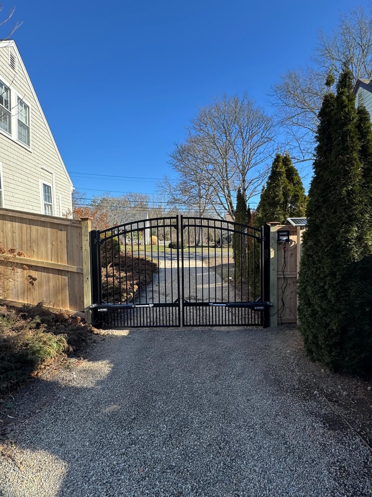 Black aluminum arched driveway gate with wood fence wings — elegant entryway